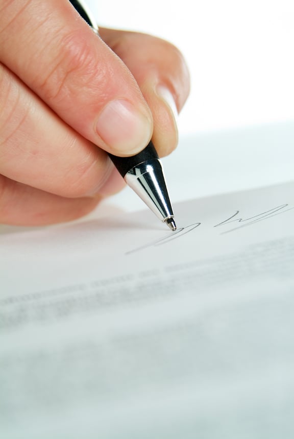Nahaufnahme einer Hand die mit einem Kugelschreiber unterschreibt